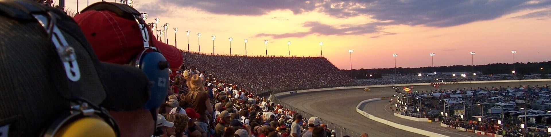 A crowded racetrack at sunset with a large audience.