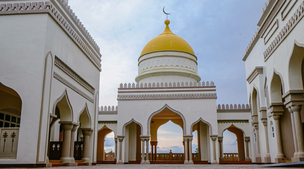 A grand mosque with a golden dome, arched walkways, and intricate architectural details.