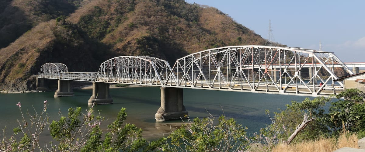 A steel truss bridge over a river with hills in the background.