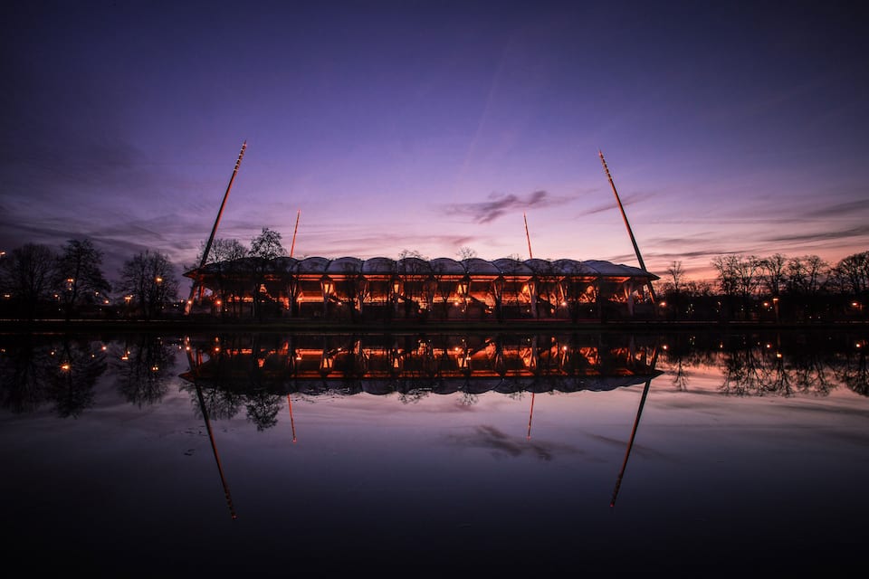 A large, illuminated building with a reflective water surface in front of it.