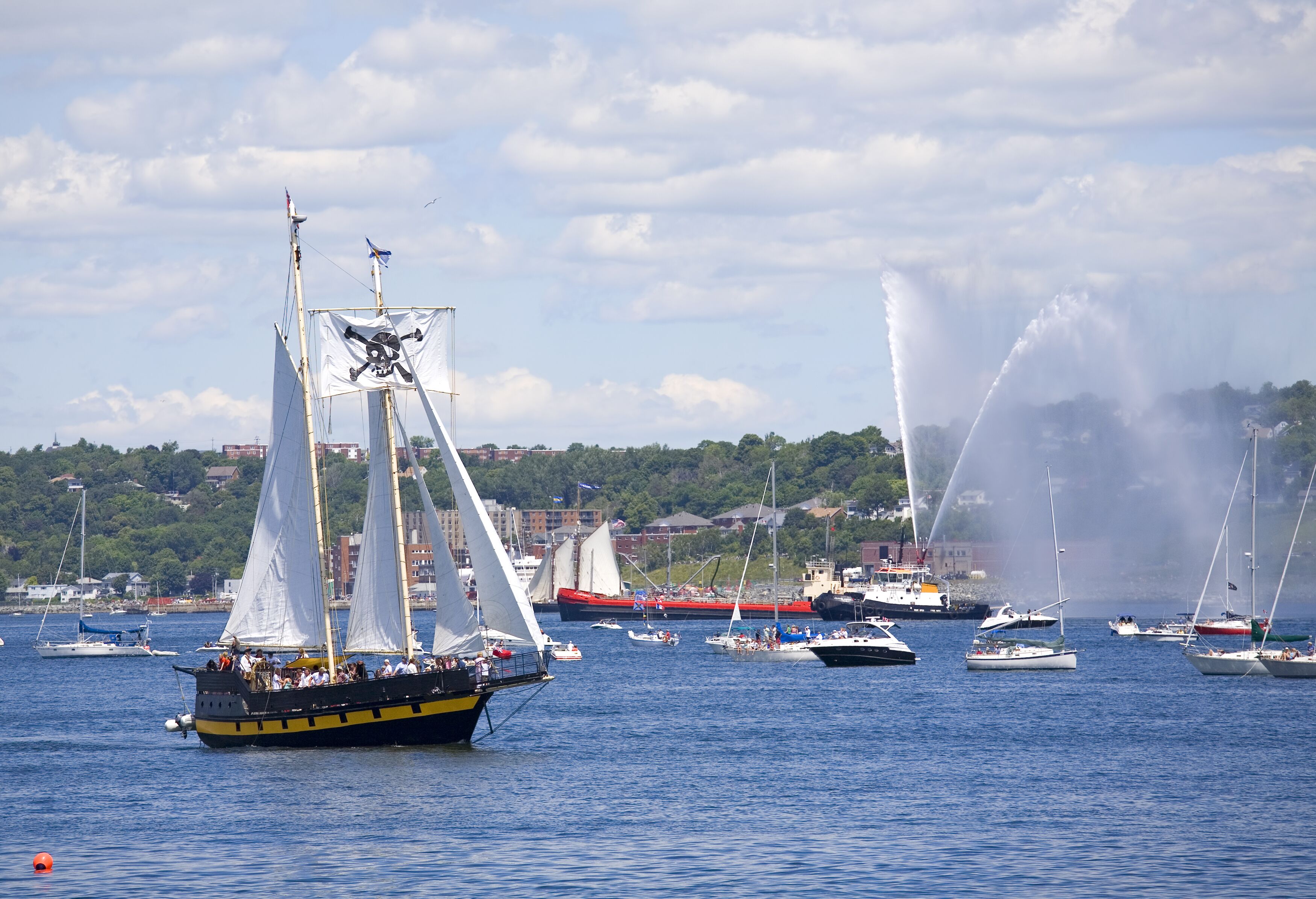 A tall ship is saluted with water cannons as she sails out of Halifax Harbour with Dartmouth in the background during the sail past of the Nova Scotia Tall Ships Festival 2009