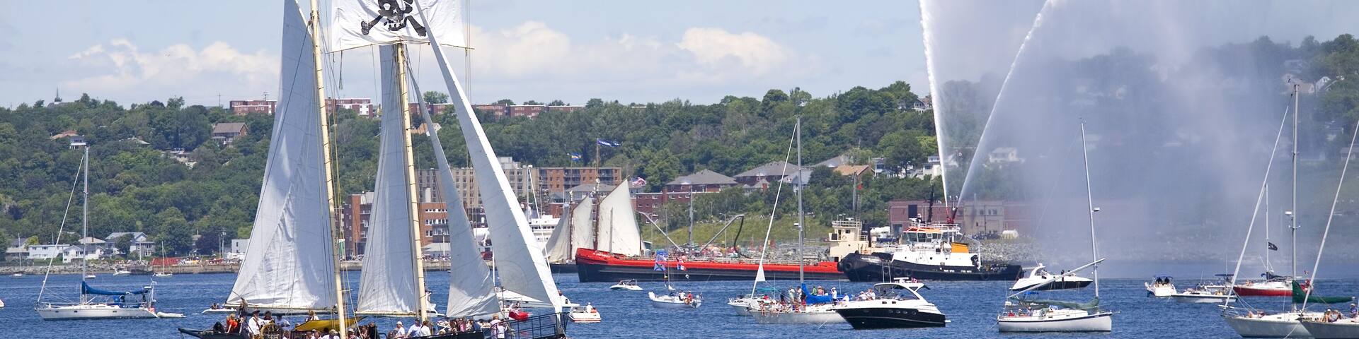 A tall ship is saluted with water cannons as she sails out of Halifax Harbour with Dartmouth in the background during the sail past of the Nova Scotia Tall Ships Festival 2009