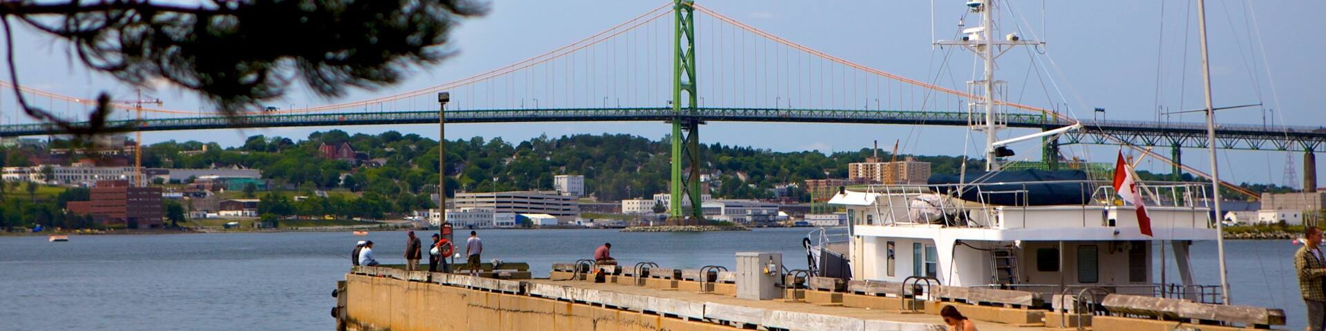 A harbor with a large green bridge in the background, a boat docked at the pier, and rocky shores.