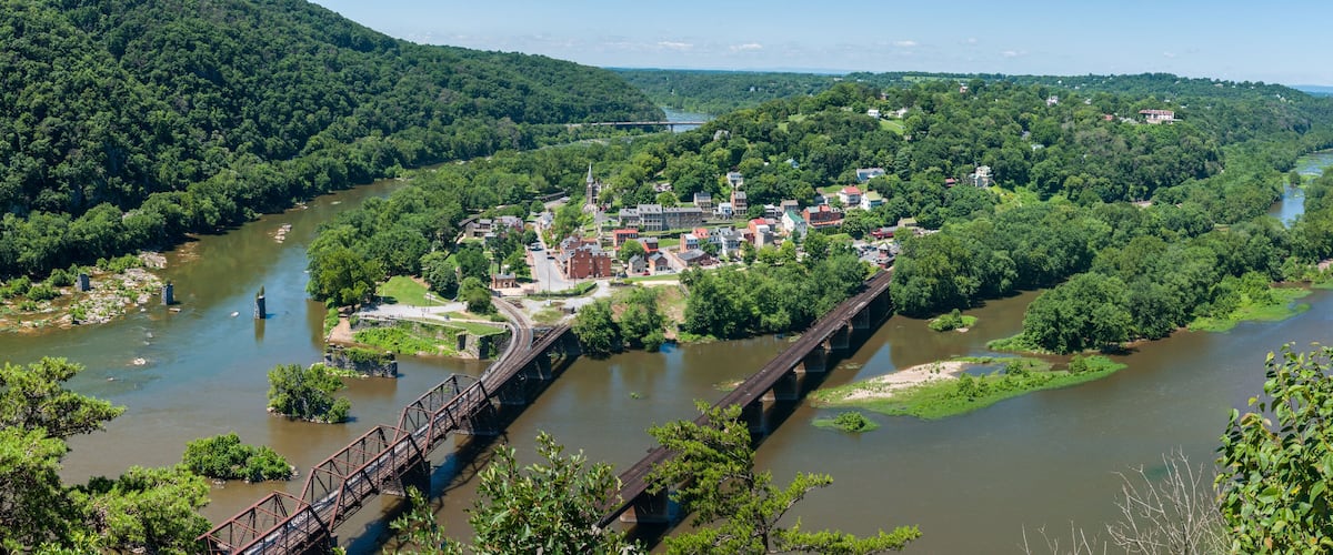 A river with a bridge, surrounded by dense greenery and a town with buildings and a church.