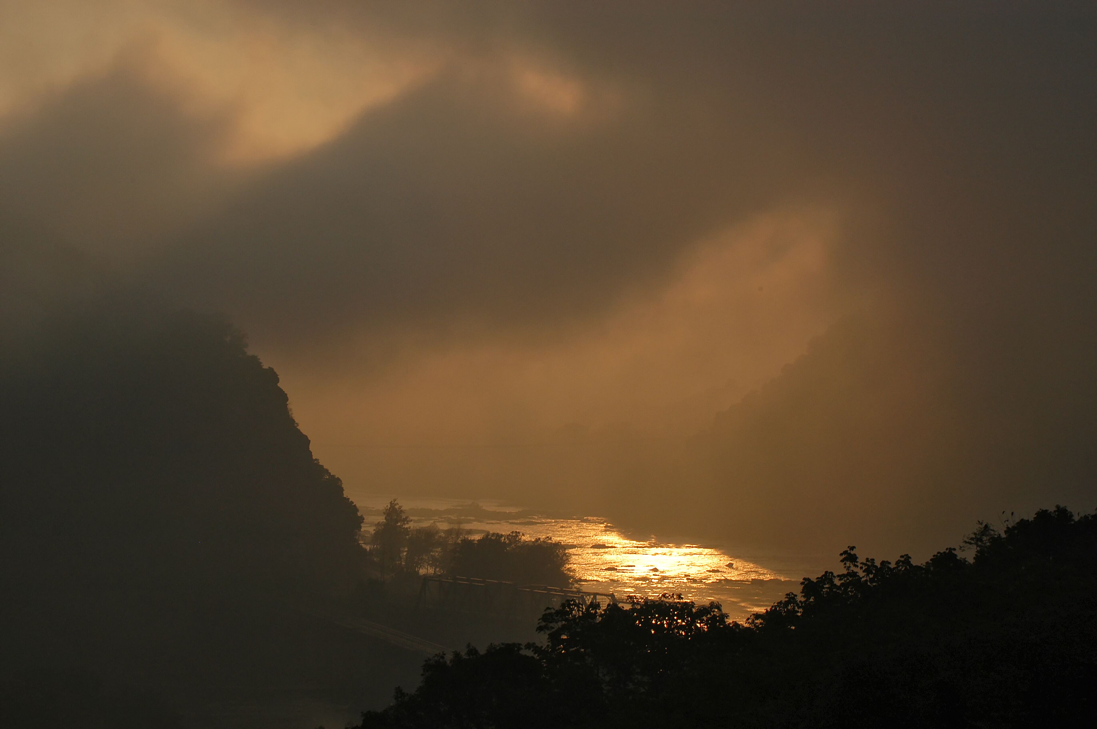 Um pôr do sol sobre uma paisagem costeira com falésias e uma ponte.