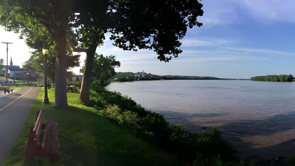 A river with a park on the right, a road on the left, and a distant island.