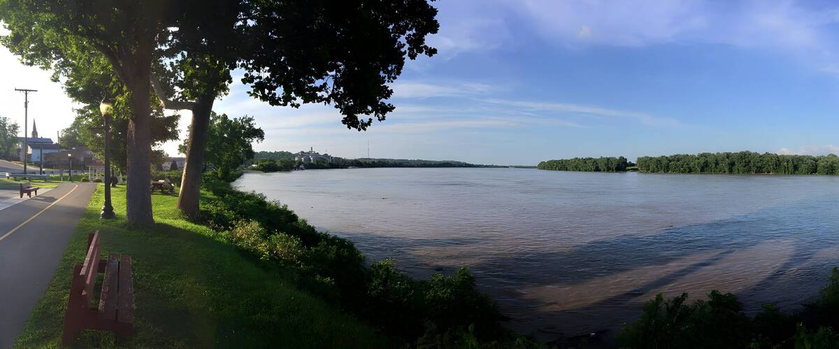 A river with a park on the right, a road on the left, and a distant island.