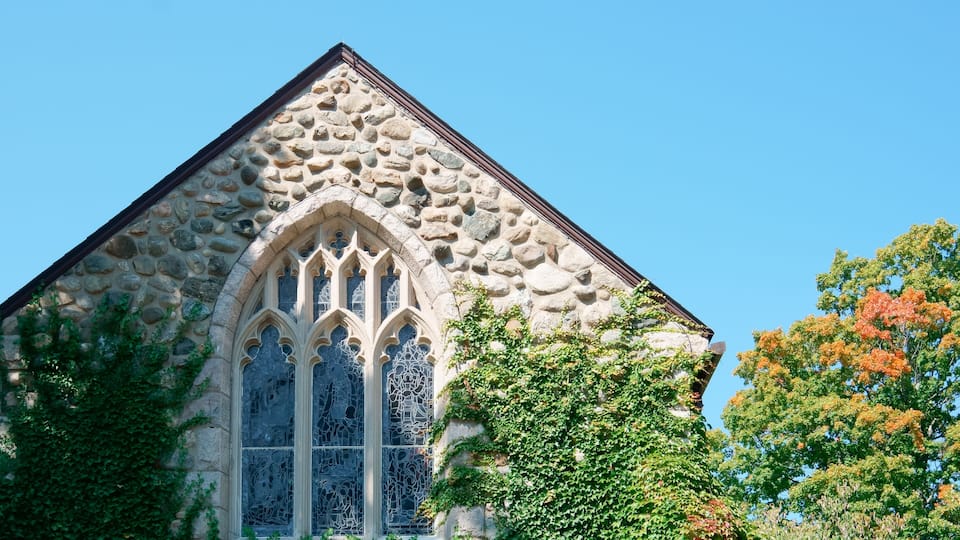 A stone church with a pointed roof and a large arched window with intricate designs.