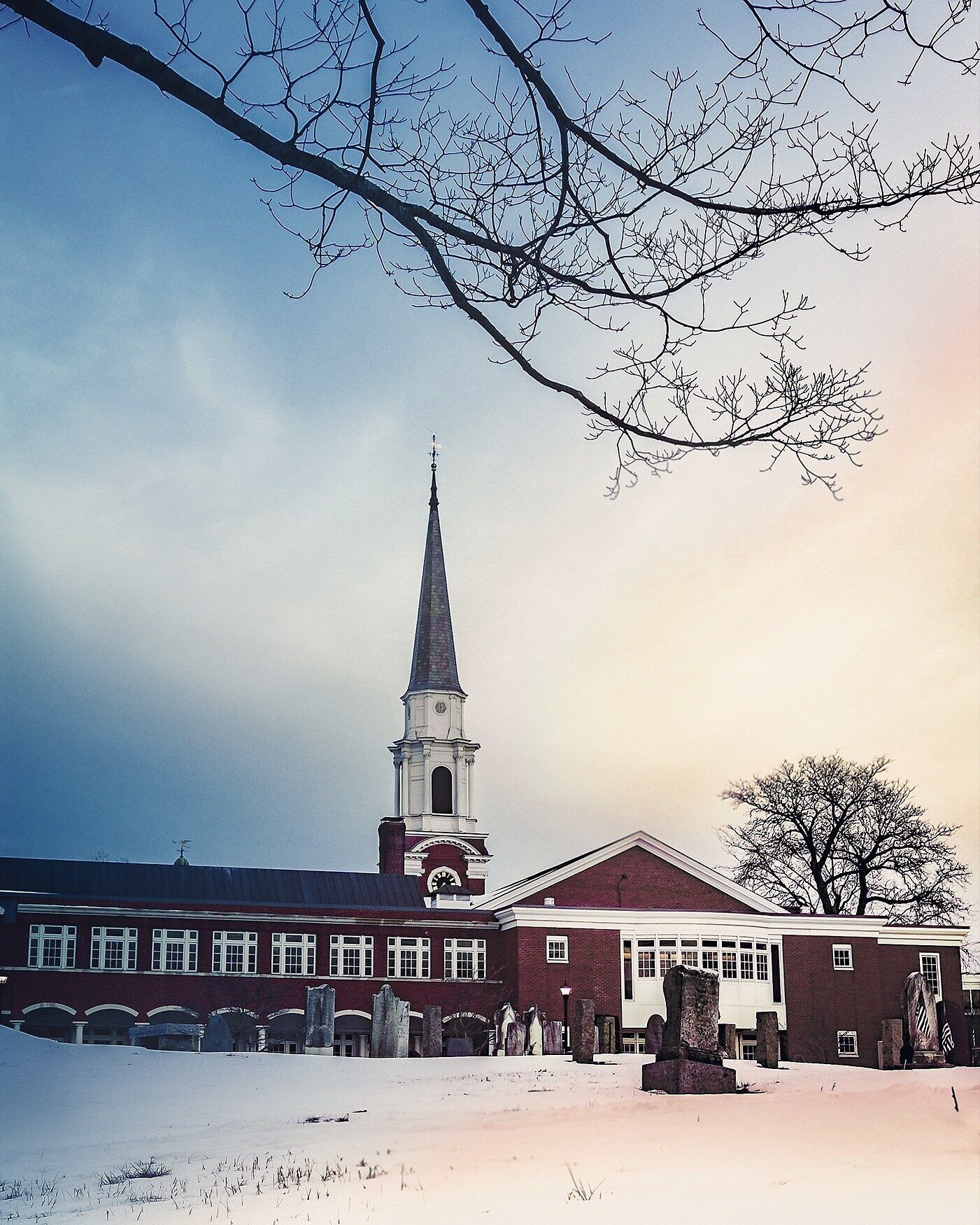 A church with a tall steeple and a cemetery in front.