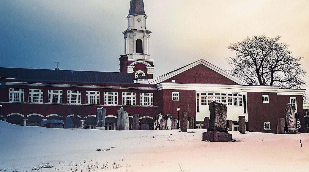 A church with a tall steeple and a cemetery in front.