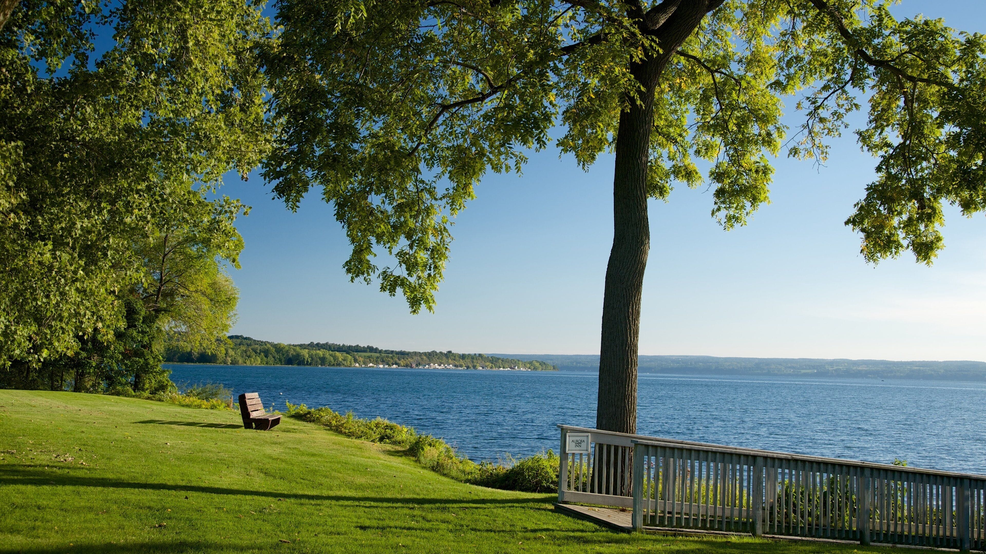 A lakeside view with a bench, a wooden fence, and a sign for Aurora Inn.