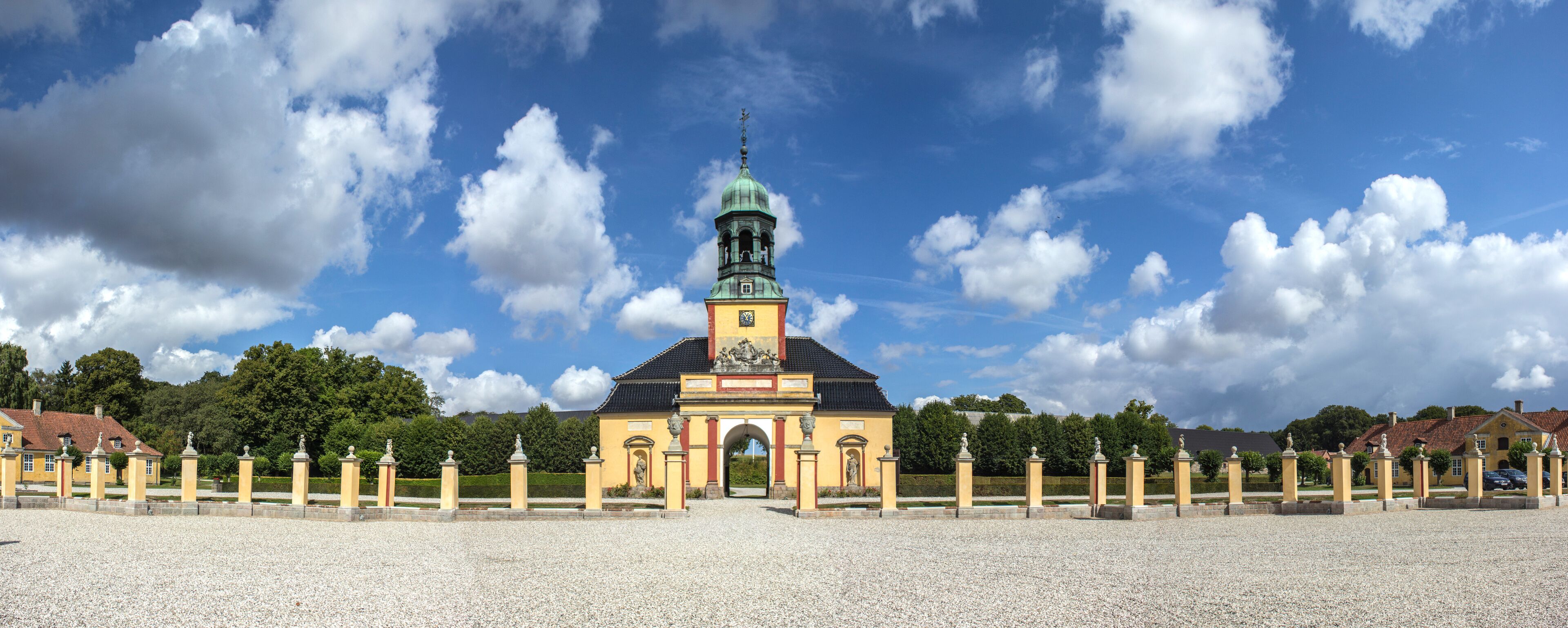 A historic building with a clock tower, surrounded by a gravel pathway and statues.