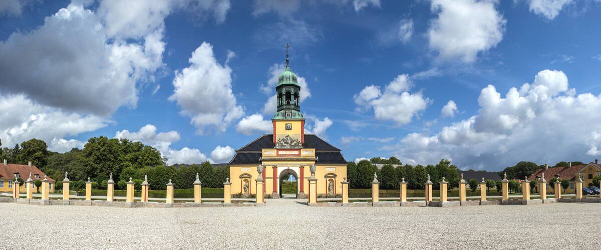 A historic building with a clock tower, surrounded by a gravel pathway and statues.