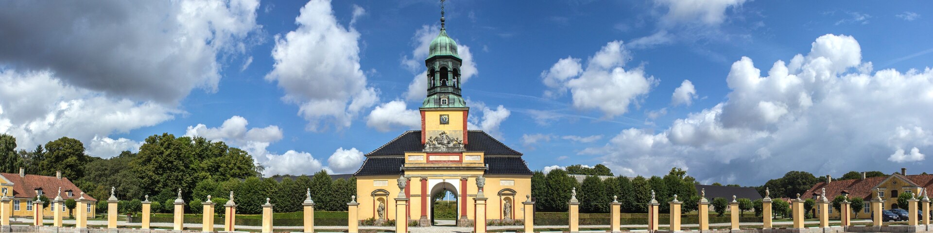 A historic building with a clock tower, surrounded by a gravel pathway and statues.