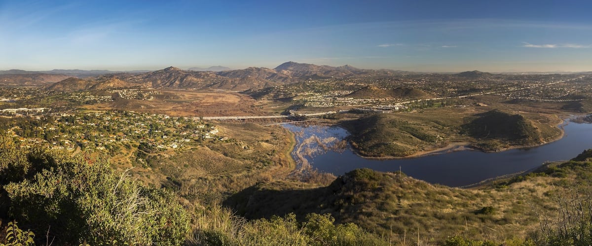 A panoramic view of a mountainous landscape with a river, a bridge, and a town.