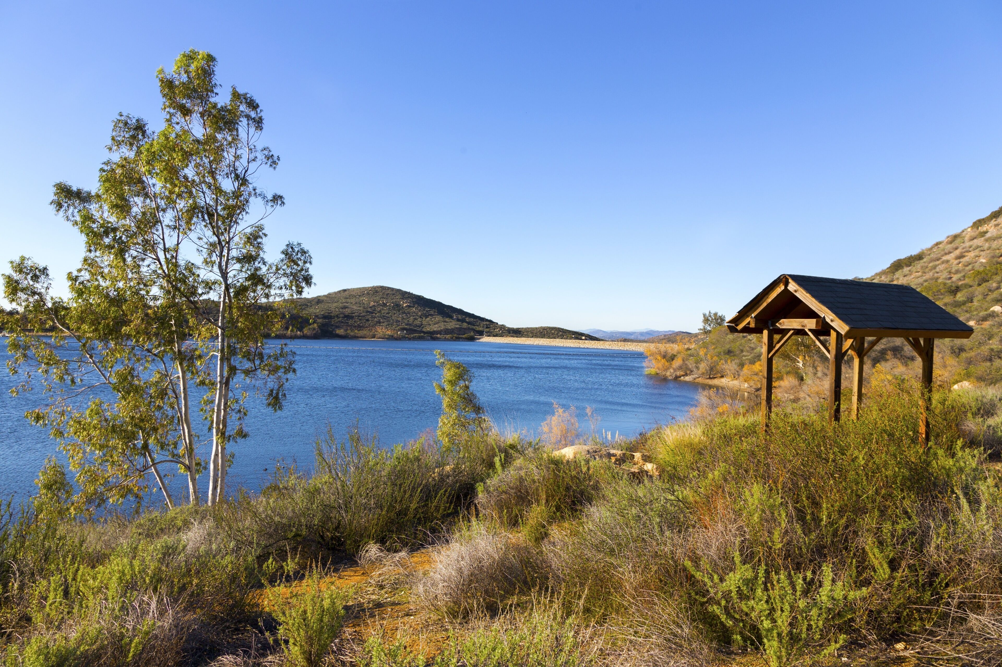 Wooden Gazebo Structure and Picnic Area at Lake Poway Hiking Trail. Scenic San Diego North County Inland Landscape with Blue Sky and Green Grassland
