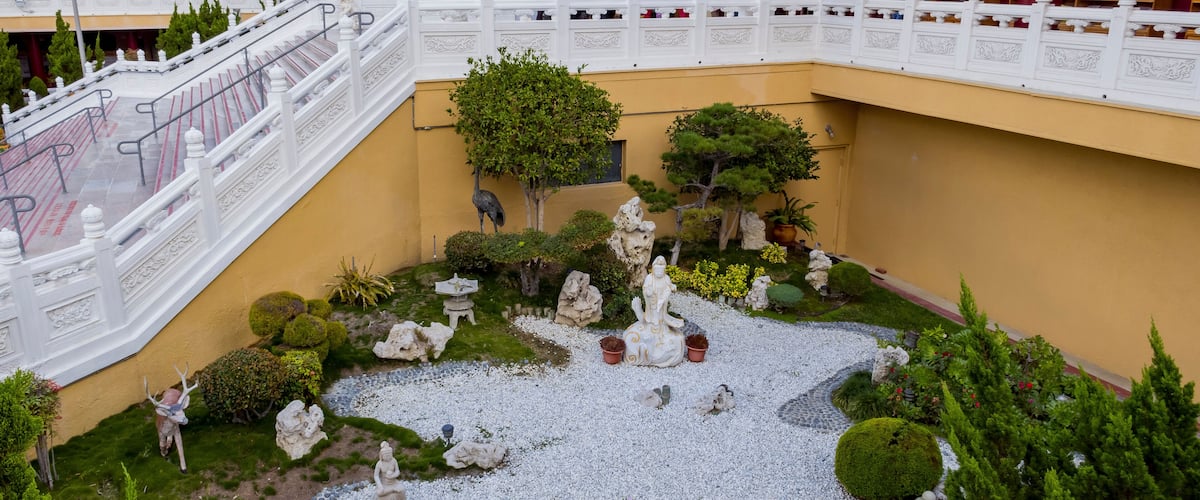 A courtyard with statues, a white railing, and a yellow wall.