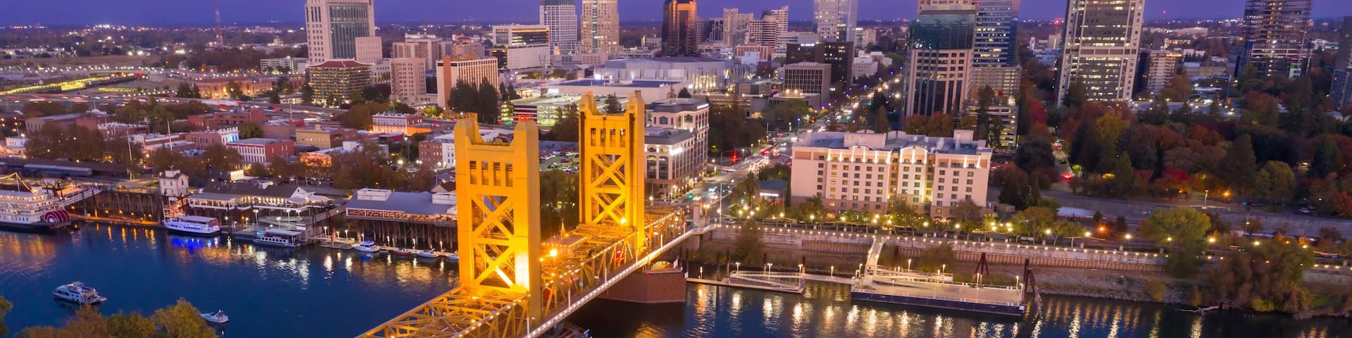 Evening view of the iconic Sacramento, CA, Bridge, illuminated at dusk. City skyline and riverfront are visible. Tower Bridge, Sacramento, California, USA