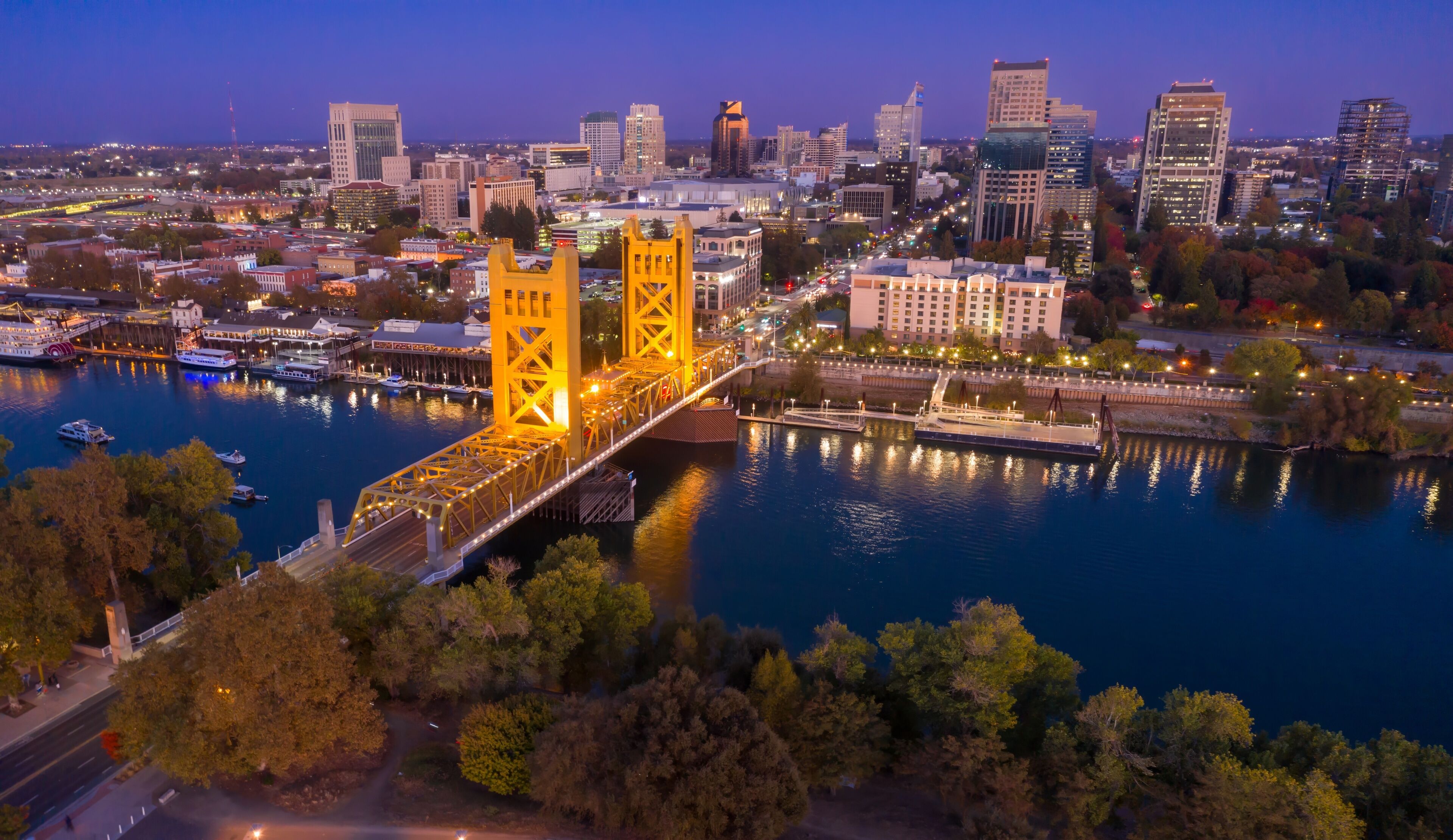A cityscape with a prominent yellow bridge over a river, surrounded by urban buildings and trees.