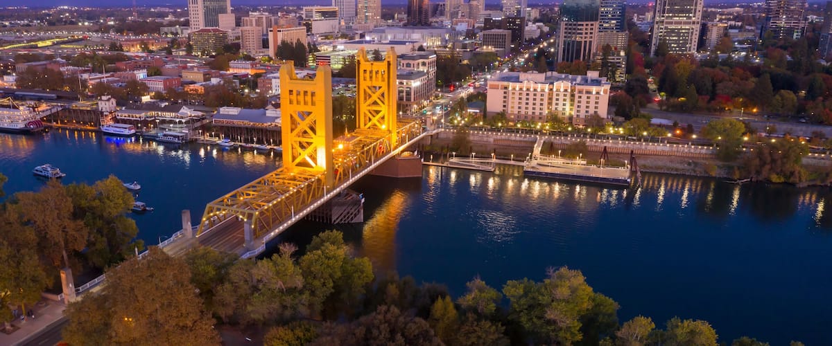 A cityscape with a prominent yellow bridge over a river, surrounded by urban buildings and trees.