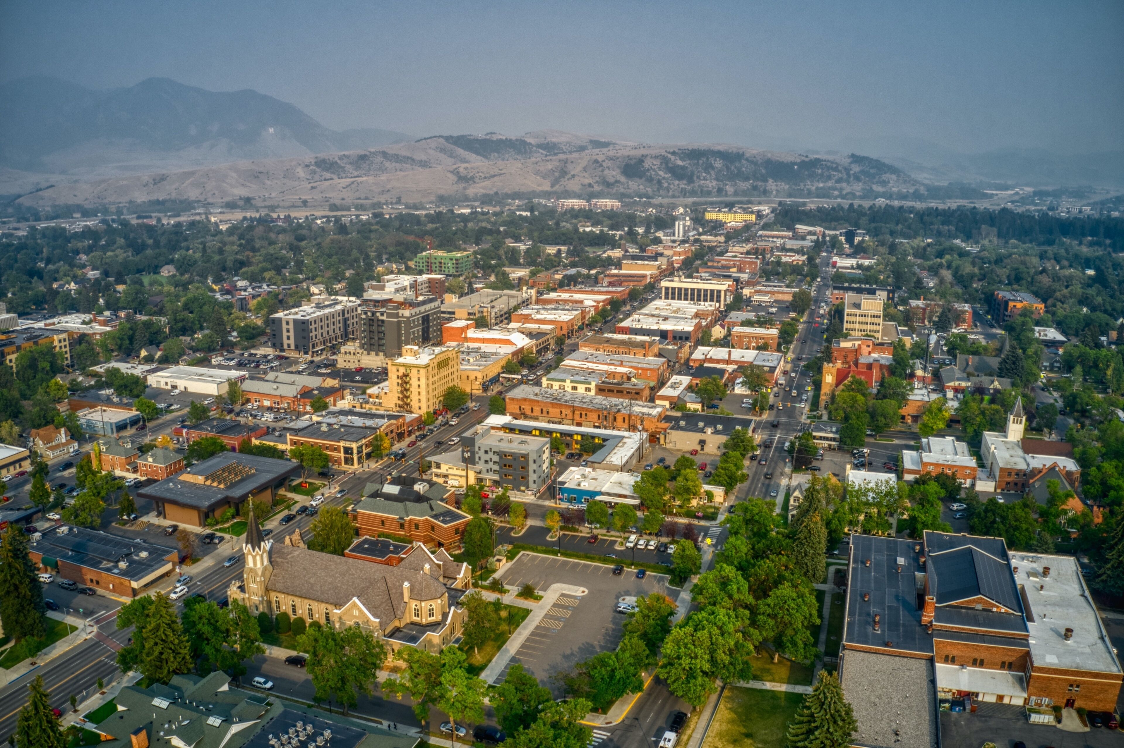 An aerial view of a town with a mix of historic and modern buildings, surrounded by green hills.