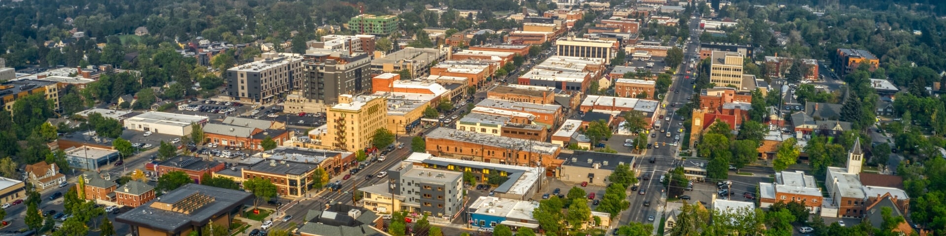 An aerial view of a town with a mix of historic and modern buildings, surrounded by green hills.