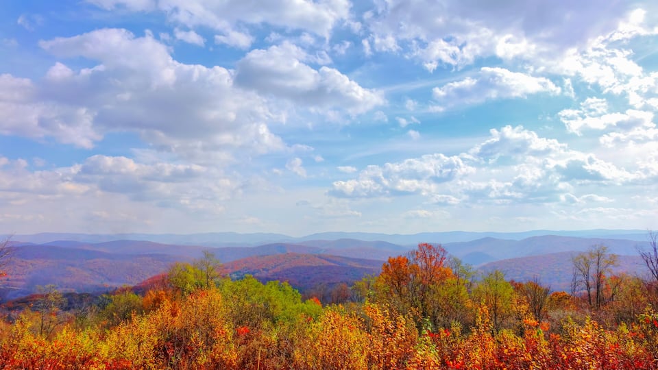 A mountainous landscape with autumn foliage and a partly cloudy sky.