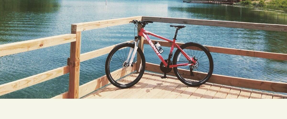 A red bicycle parked on a wooden dock by a calm lake with a wooden railing.