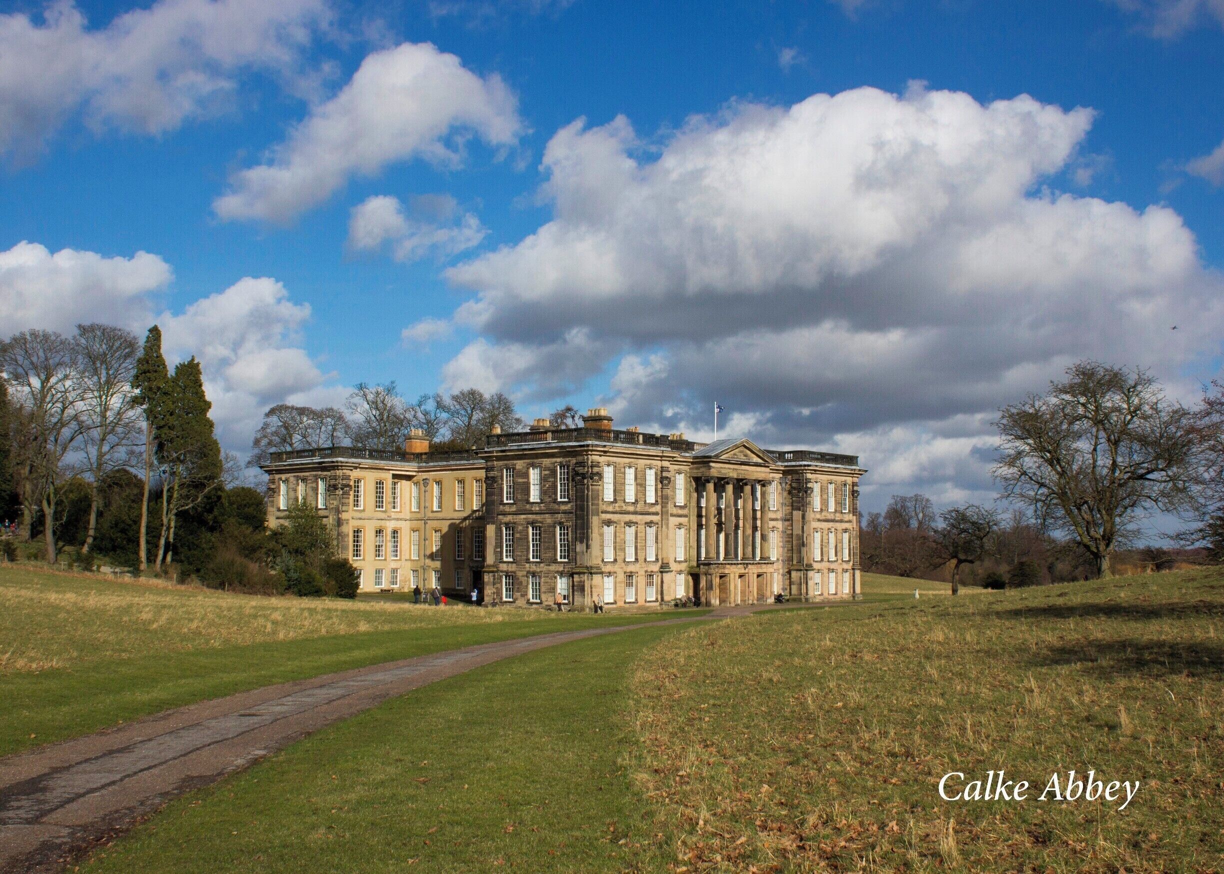 Calke Abbey, a large historic building with classical architecture, surrounded by a grassy landscape and trees.