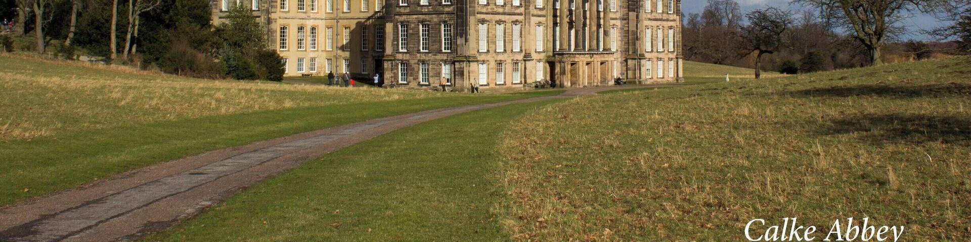 Calke Abbey, a large historic building with classical architecture, surrounded by a grassy landscape and trees.