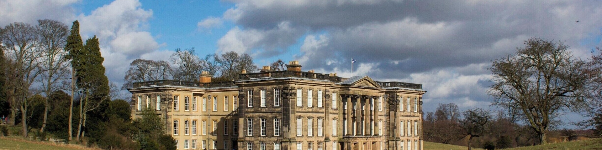 Calke Abbey, una extensa construcción histórica con arquitectura clásica, rodeada por un paisaje cubierto de césped y árboles.