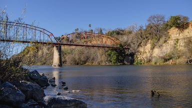 Uma ponte de metal sobre um rio com margens rochosas e vegetação escassa.