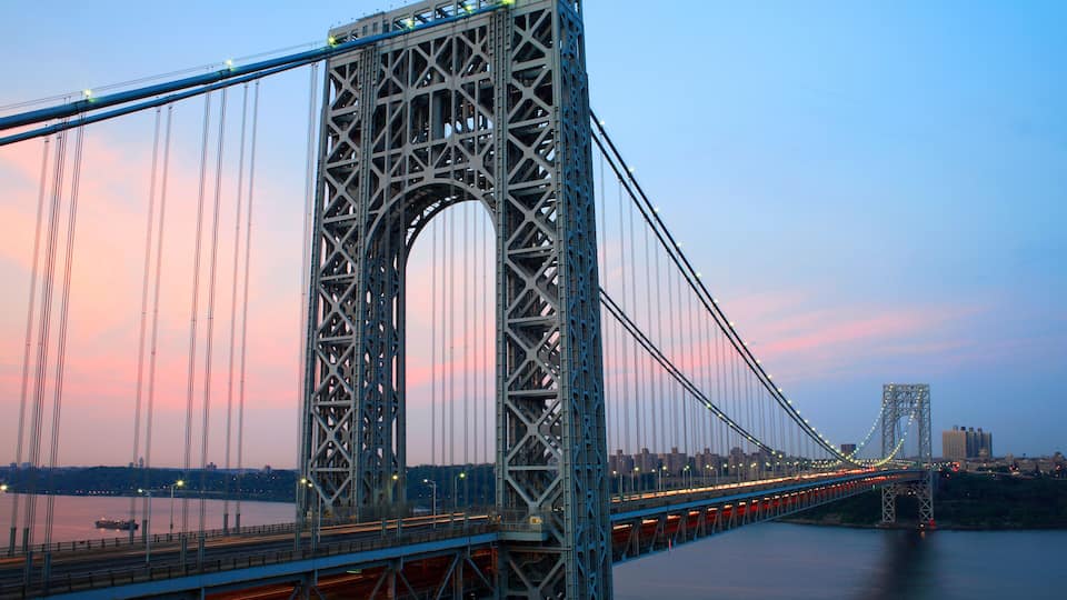 A large suspension bridge with a central arch, spanning a body of water with cityscape in the background.