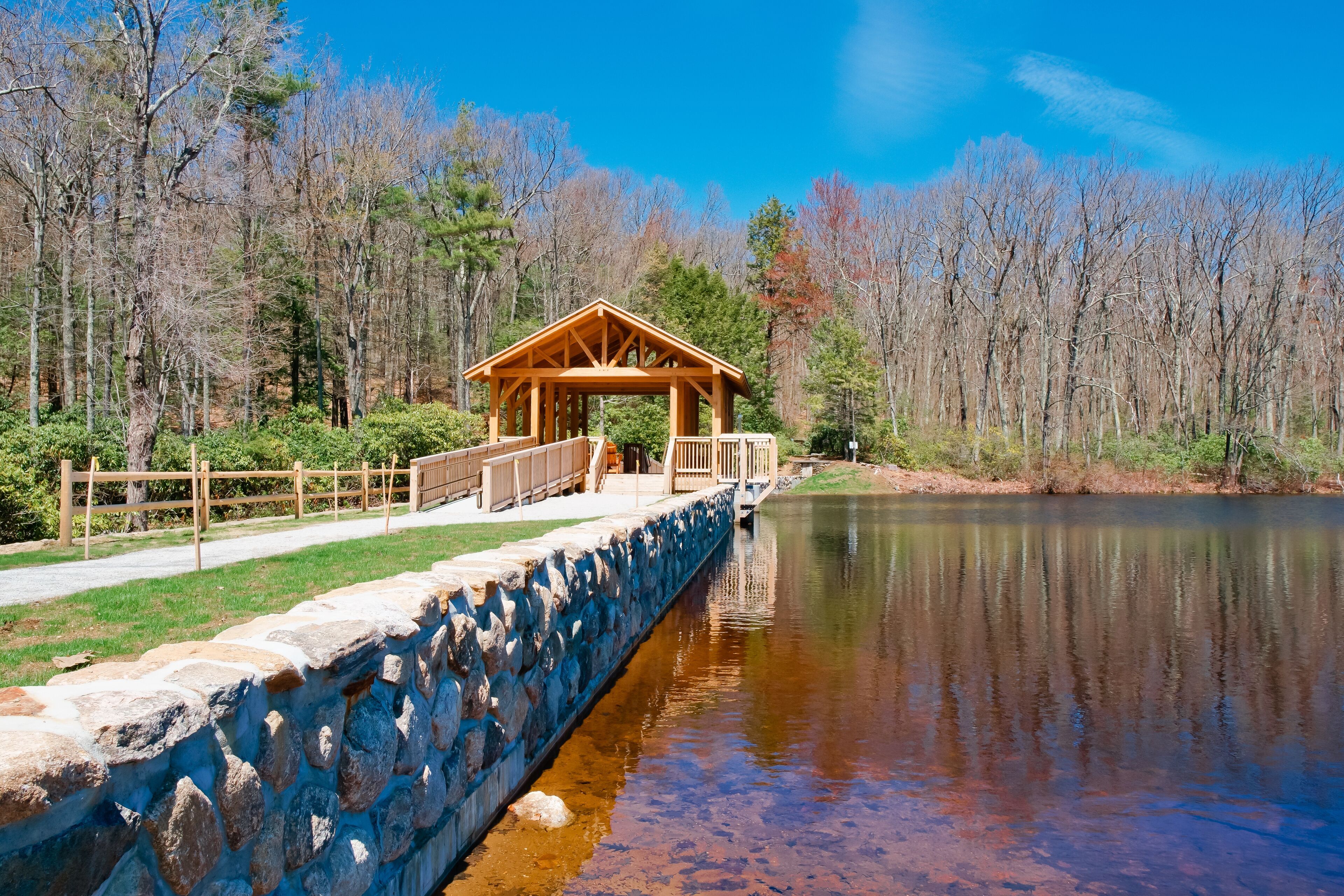 A wooden gazebo by a calm lake surrounded by trees.