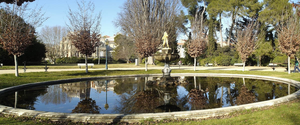 A park with a circular pond, benches, and a statue.