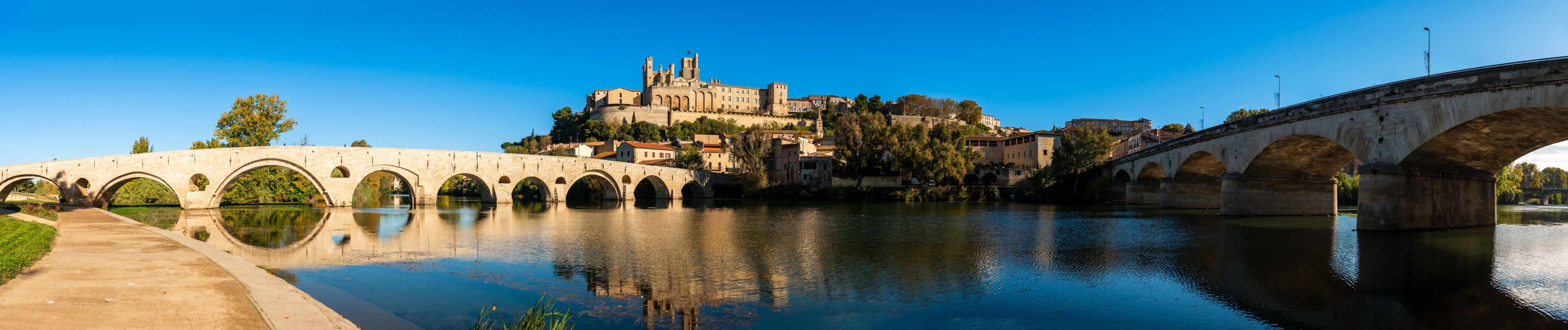 A stone bridge over a river, a historic castle on a hill, and a clear blue sky.