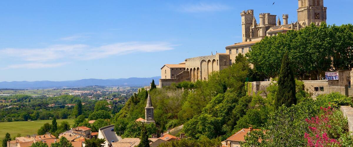 A historic castle with towers and a clock tower, surrounded by lush greenery and a distant view of the countryside.
