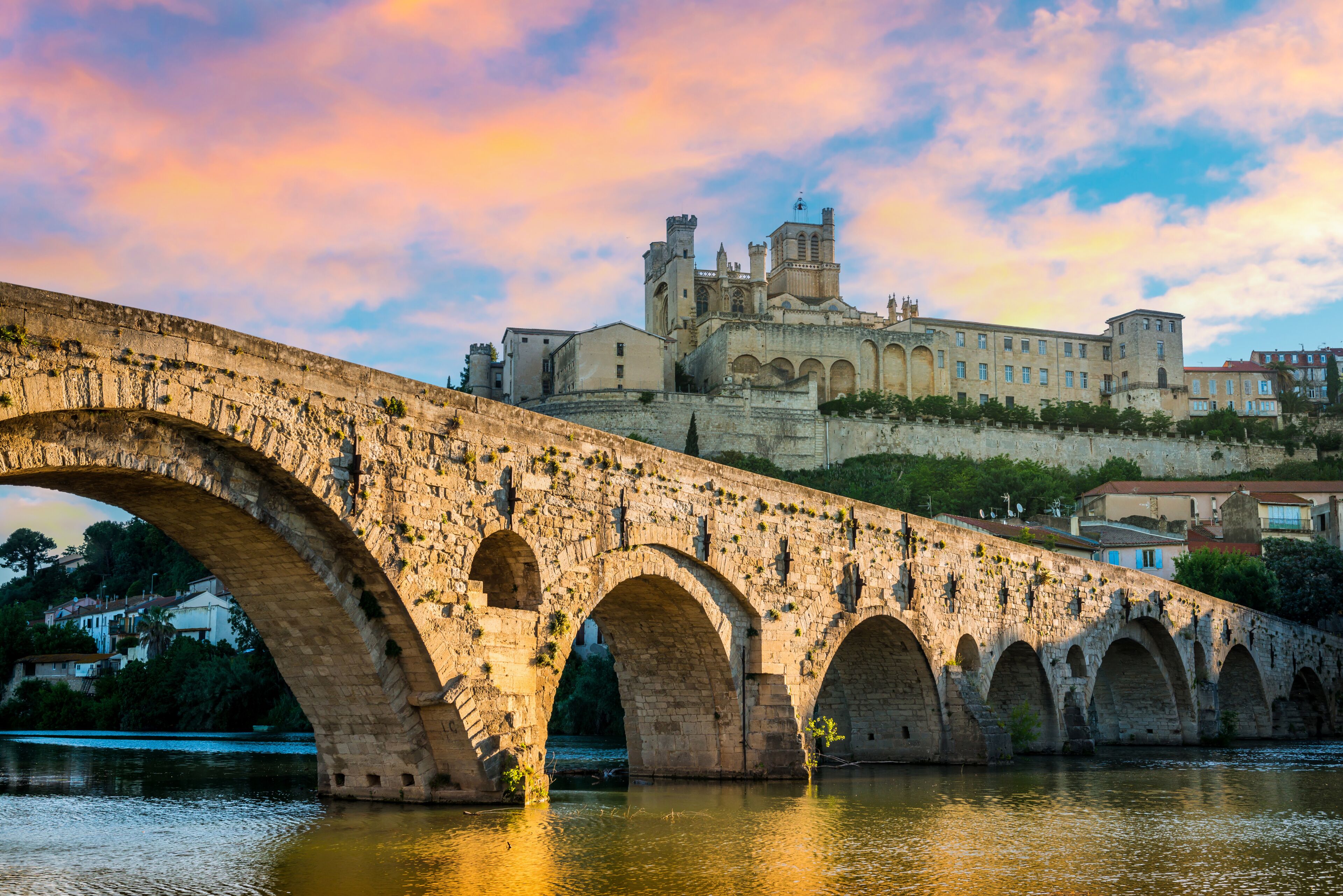 A stone bridge with arches over a river, leading to a historic building with towers.