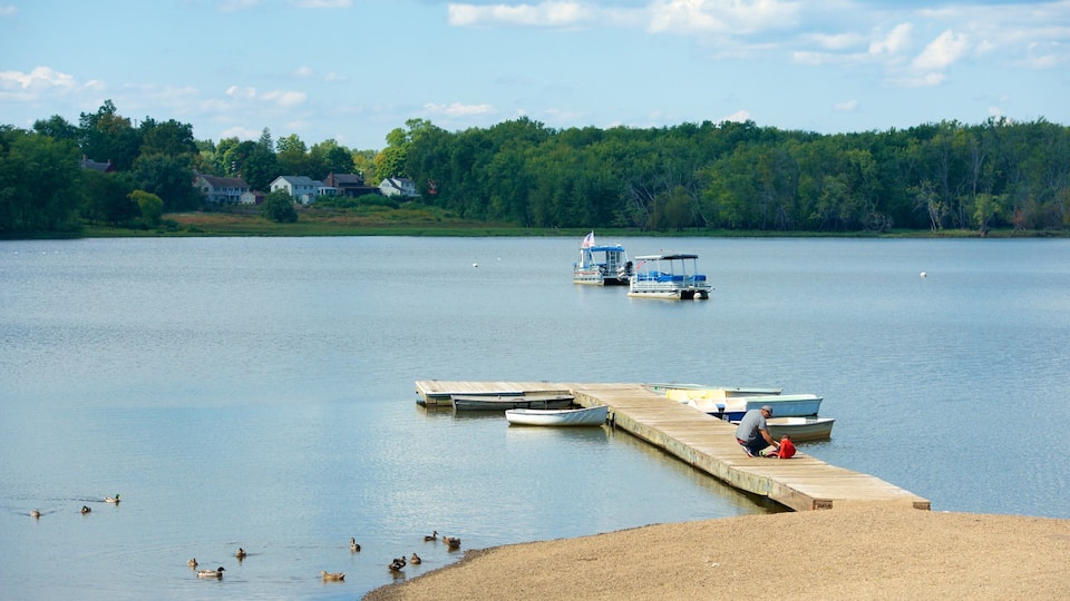 A calm lake with a wooden dock extending into the water, surrounded by a forested shoreline and several boats.