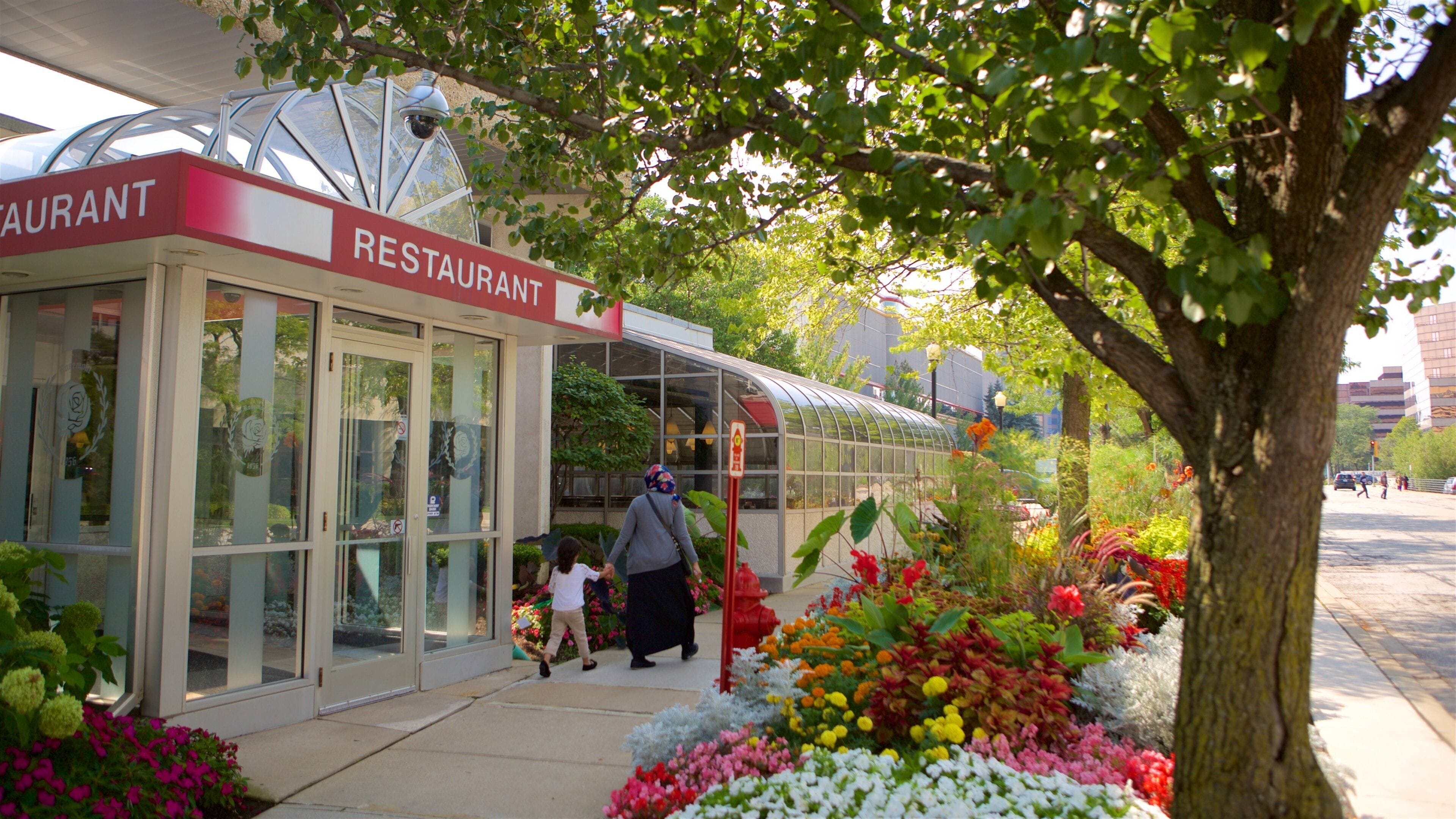 Un restaurante con fachada de vidrio y un jardín lleno de flores coloridas.