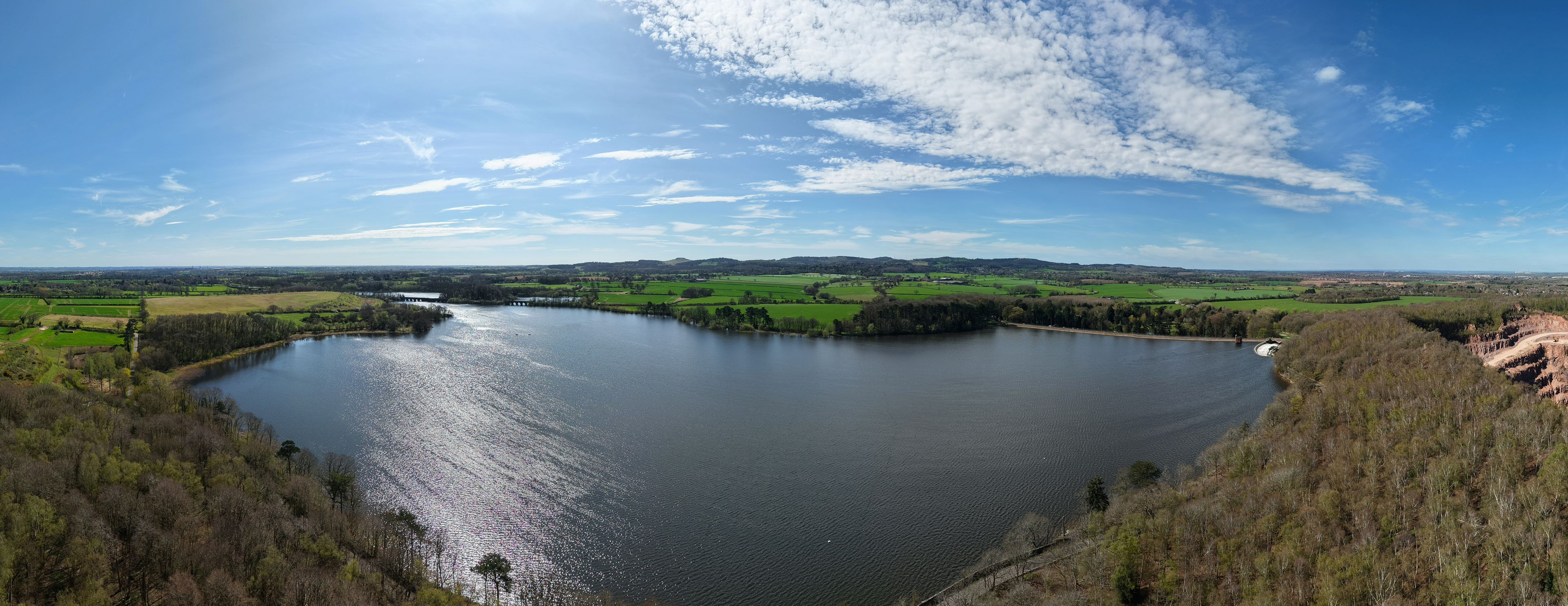 A river winding through a green landscape with hills in the distance and a partly cloudy sky.