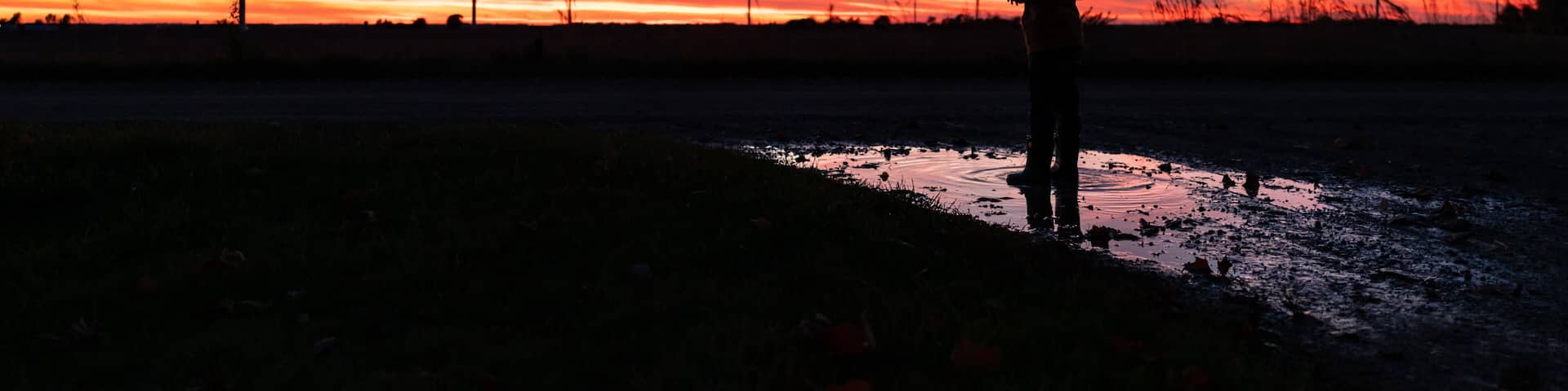 A silhouette of a person standing in a field with wind turbines in the background during sunset.