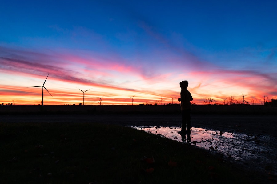 silhouette of a boy standing in a puddle on a wind farm during sunset