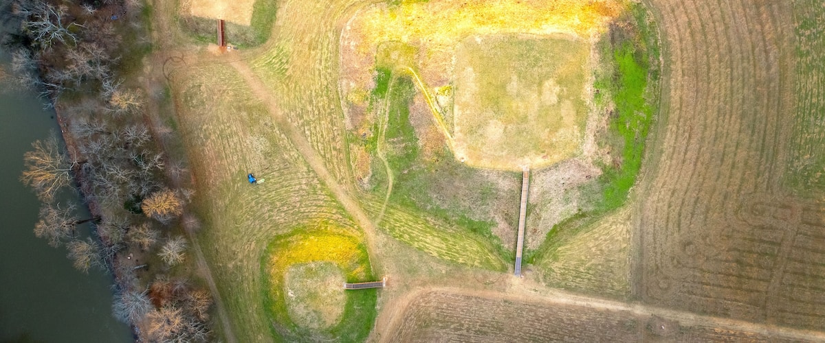 An aerial view of a field with distinct circular patterns, a small pond, and a bridge.