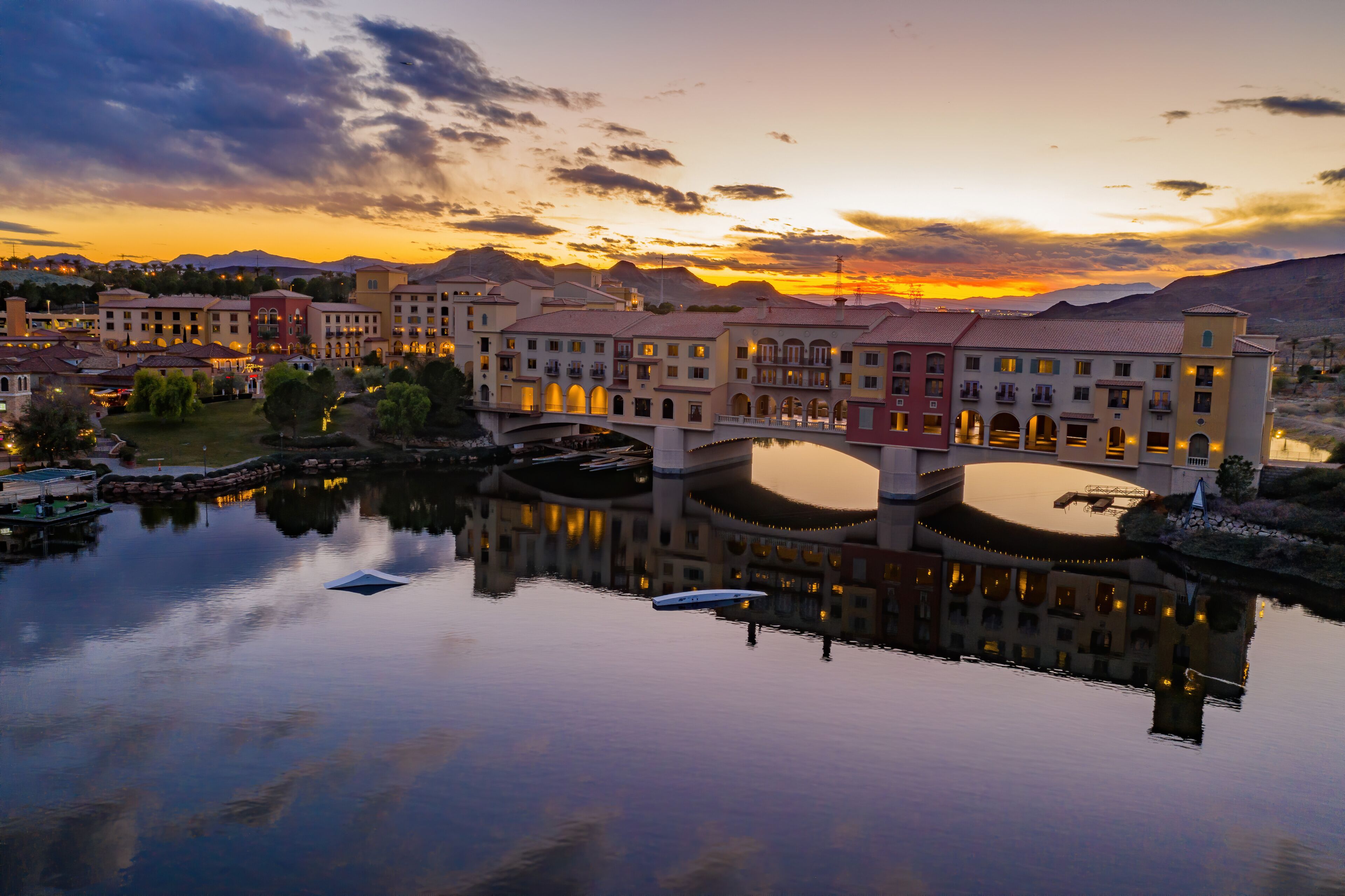 A lakeside resort with a bridge, buildings, and mountains in the background.