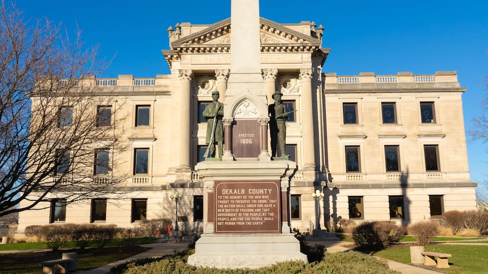 A neoclassical courthouse with a central monument, columns, and a clear blue sky.