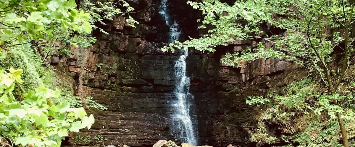A waterfall cascading over a rocky cliff surrounded by lush greenery.