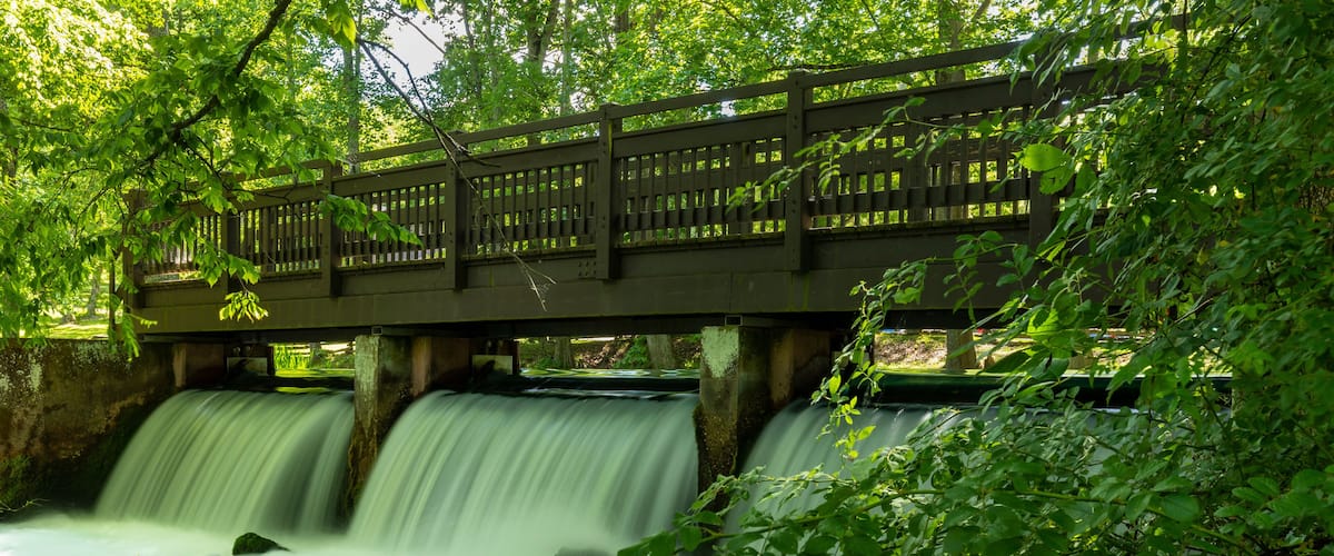 A wooden bridge over a flowing river with moss-covered rocks.