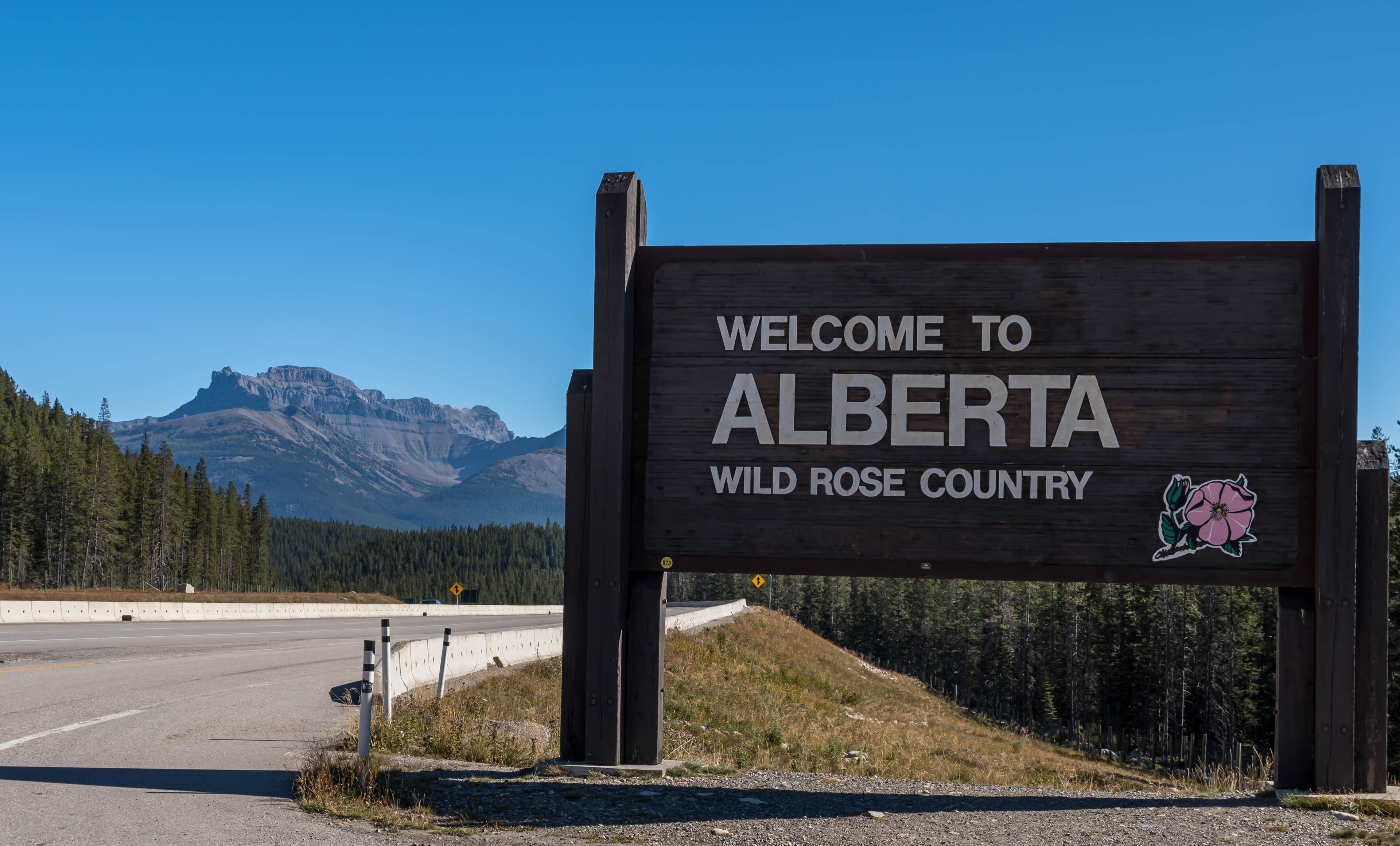 A welcome sign for Alberta with a mountain in the background.