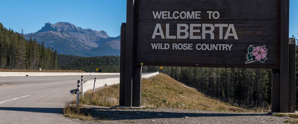 A welcome sign for Alberta with a mountain in the background.